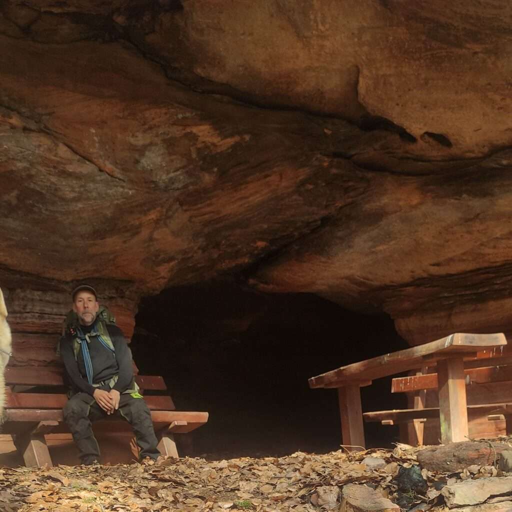 Mensch sitzt auf einer Bank vor einer Höhle